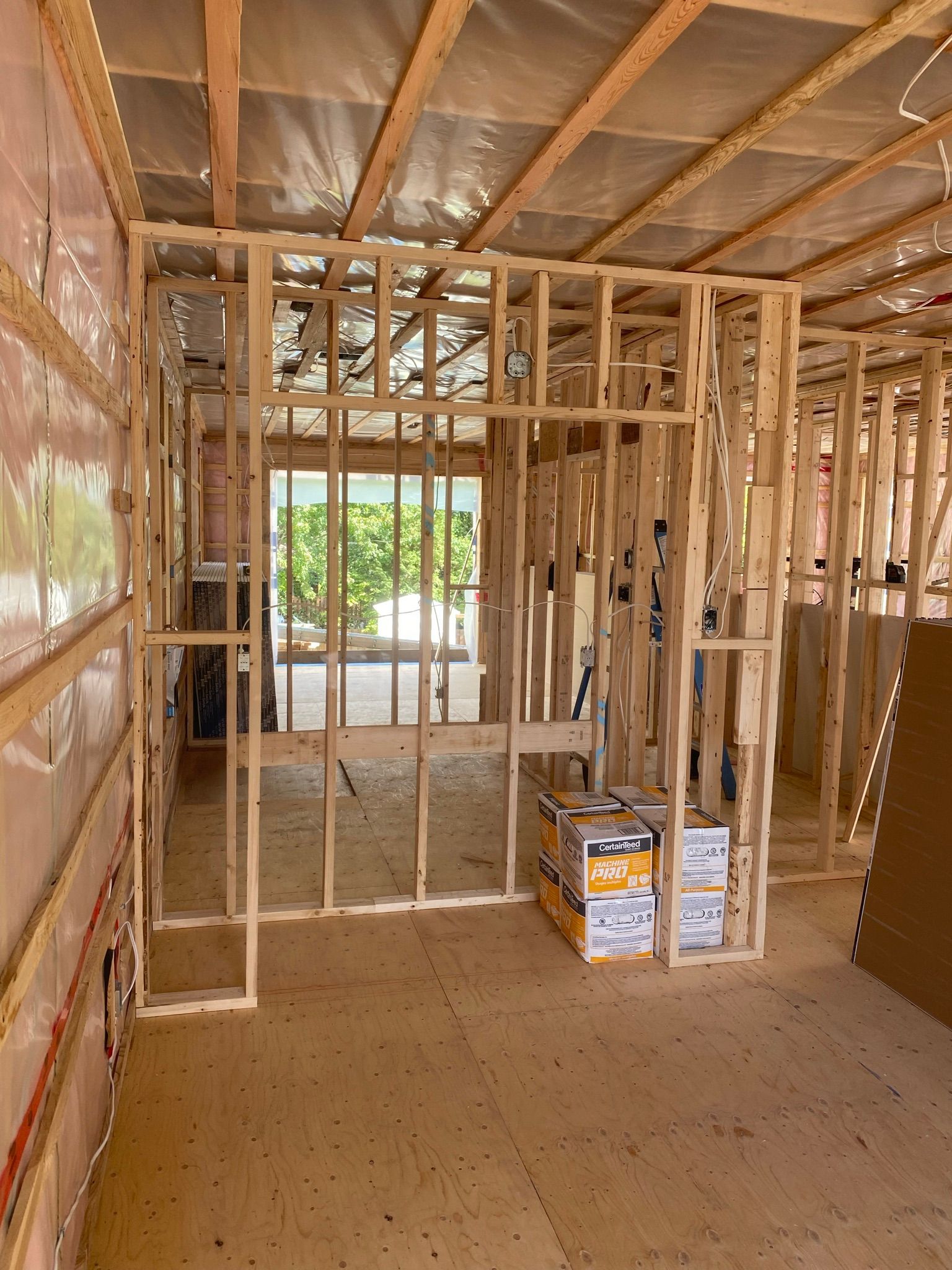 Ossature bois intérieure d'un bâtiment en construction, montrant les cloisons et une porte extérieure.