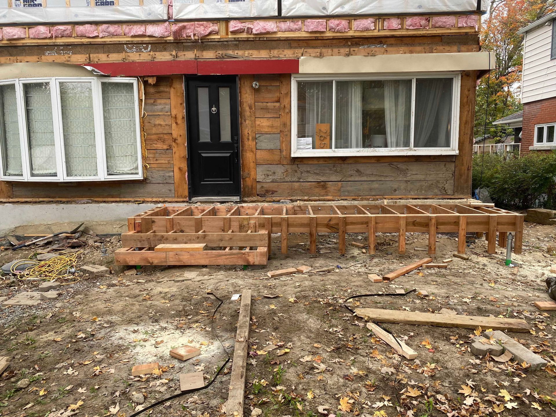 Maison en construction, avec charpente apparente pour la terrasse et les marches ; bardage brun, fenêtres.