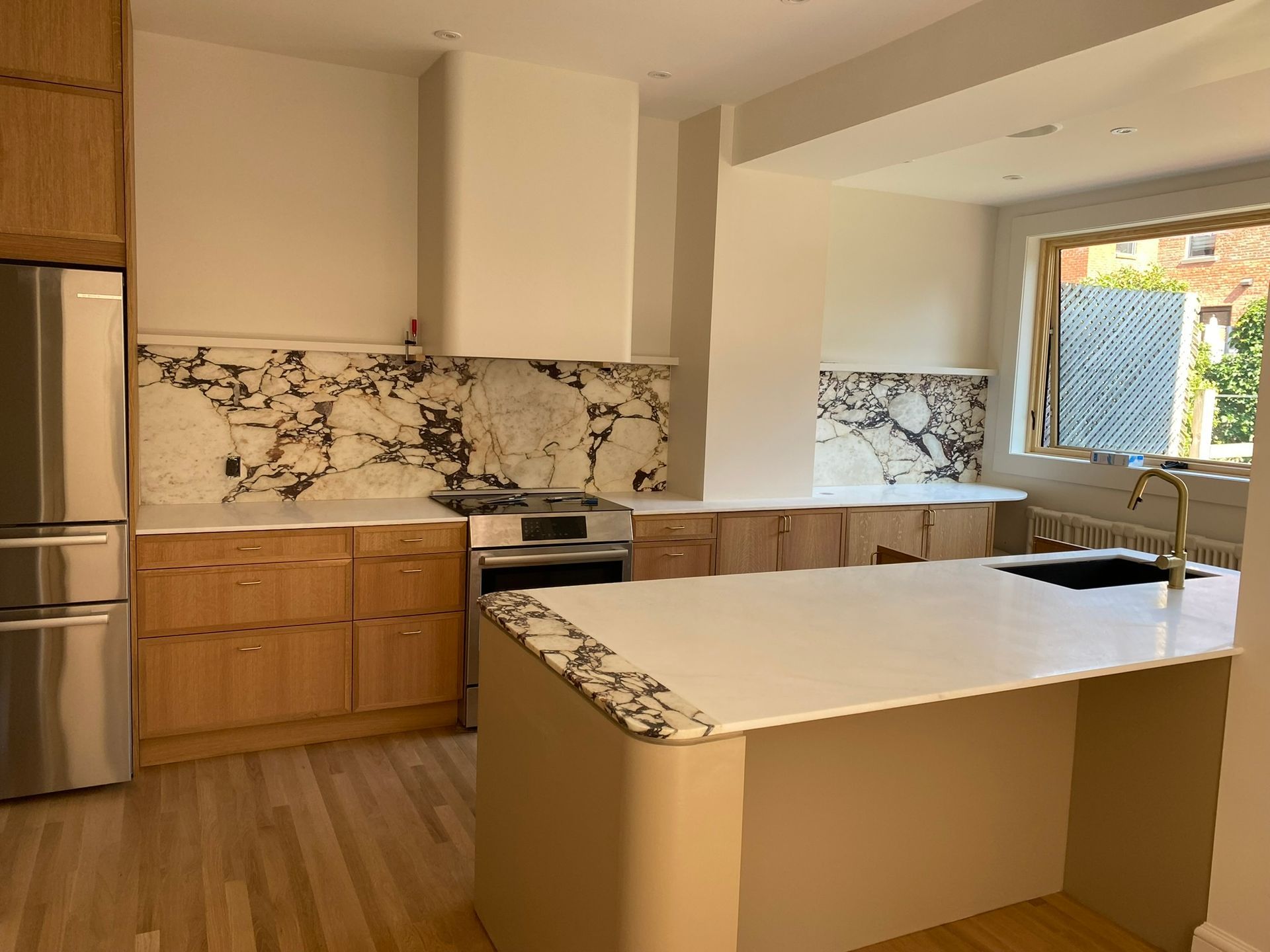 Cuisine moderne avec crédence en marbre, îlot central, placards en bois et réfrigérateur en acier inoxydable.