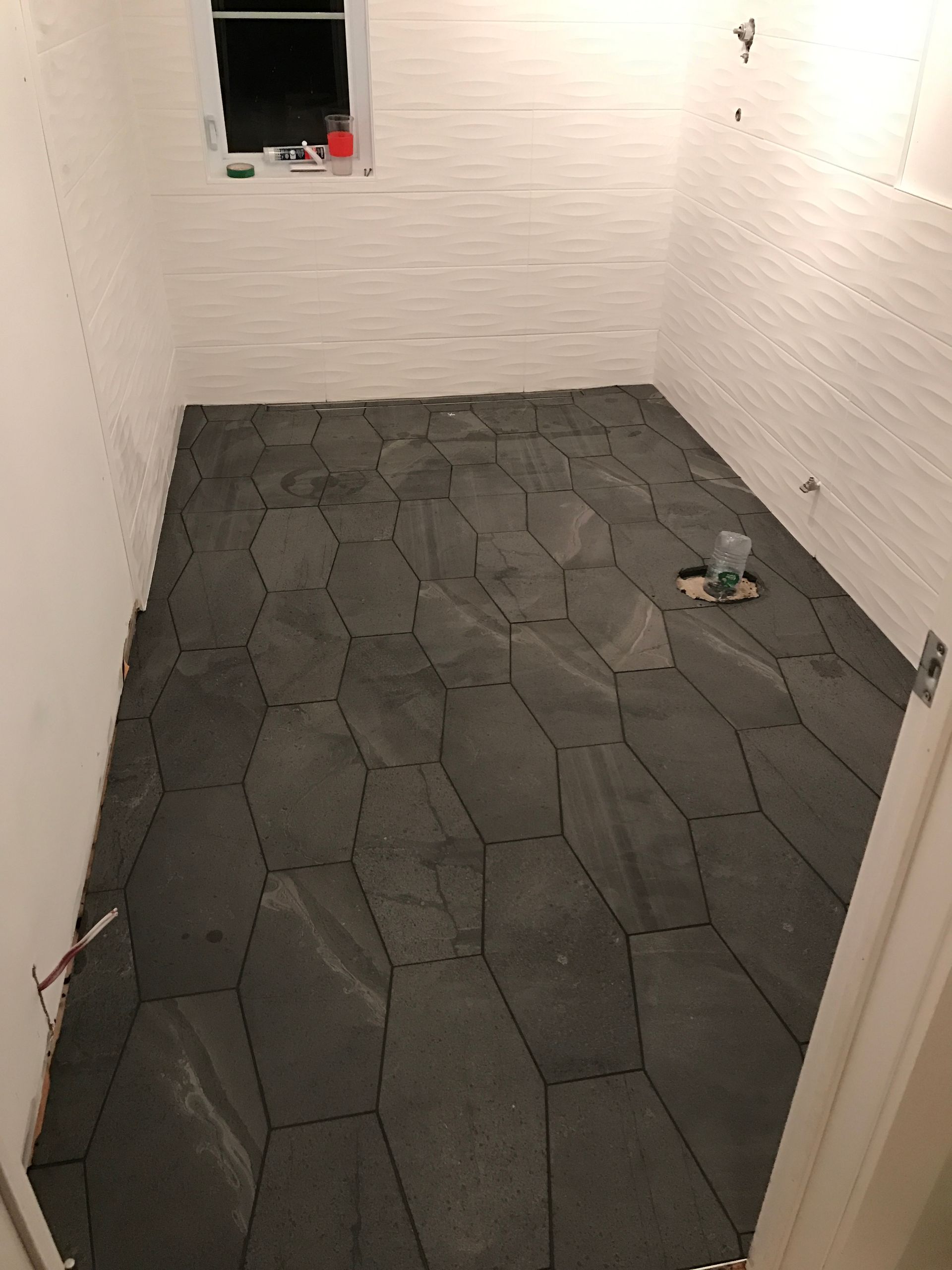 Salle de bains avec carrelage au sol gris foncé de forme irrégulière, carrelage mural blanc imitation brique et une petite fenêtre.