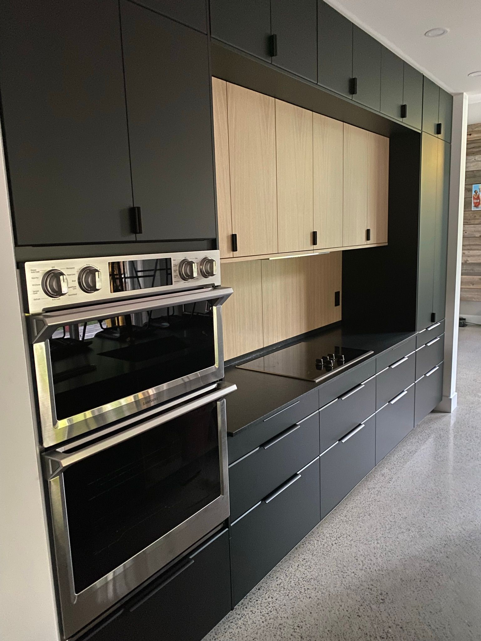 Cuisine moderne avec armoires noires, four en acier inoxydable et touches de bois clair.
