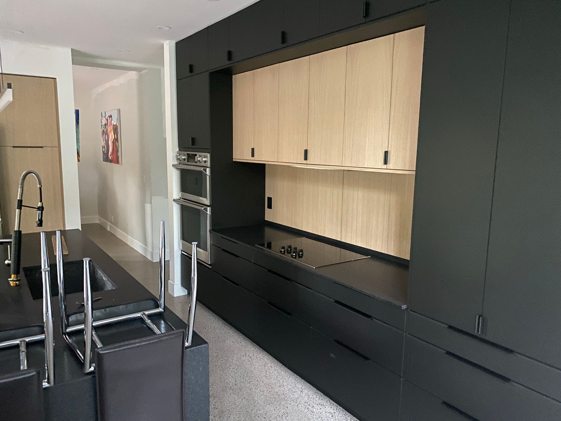 Cuisine moderne avec armoires noires, armoires hautes en bois clair, appareils électroménagers intégrés et comptoir noir.