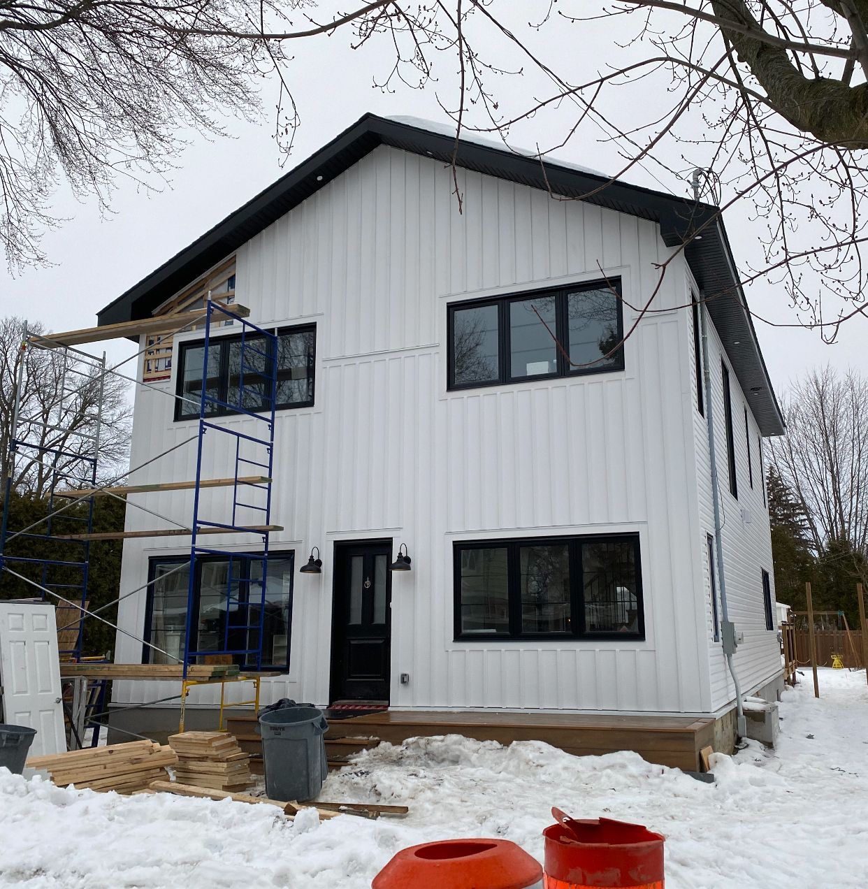 Maison blanche de deux étages en construction, avec fenêtres et toit noirs, dans un décor enneigé.