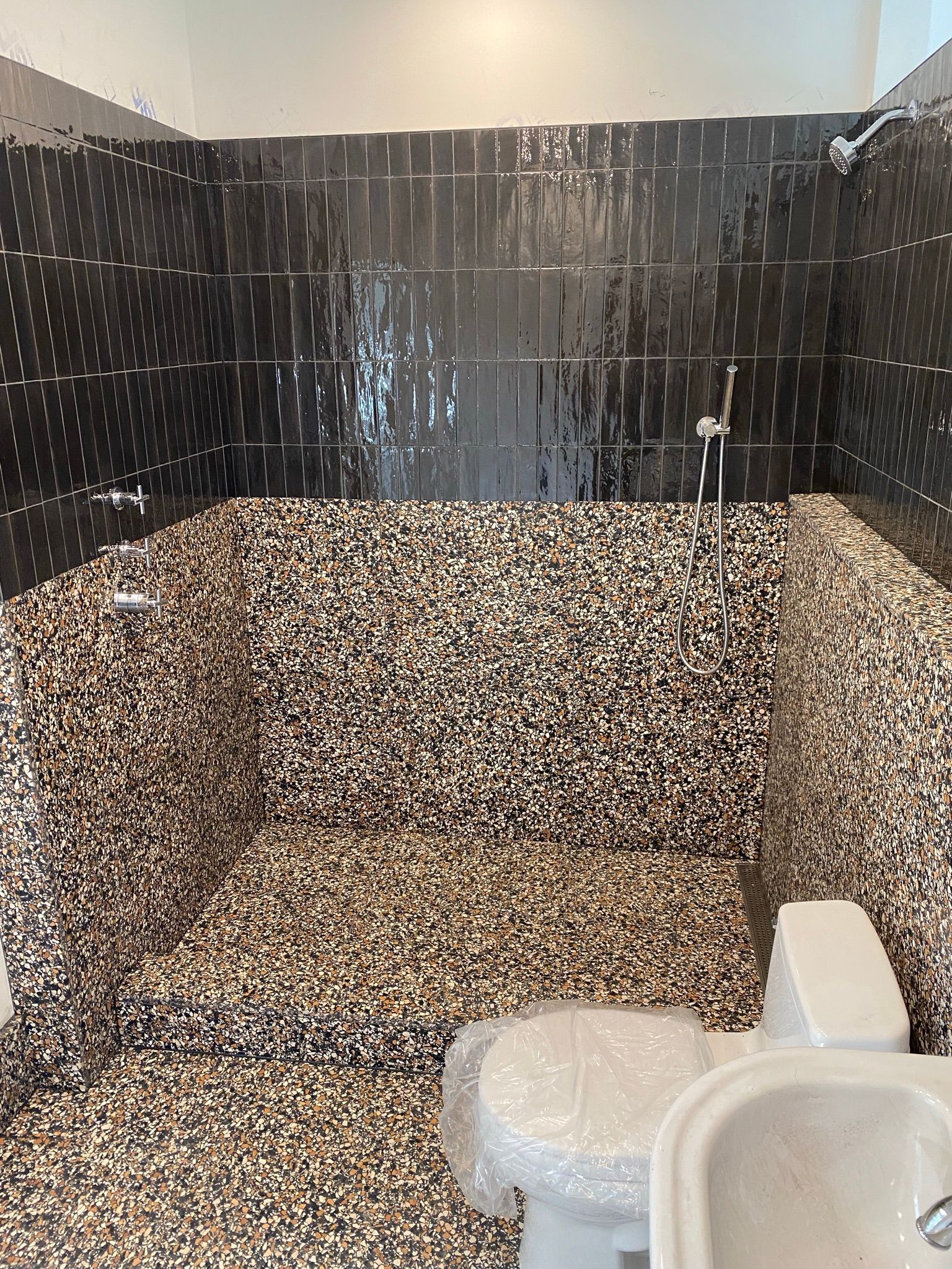 Salle de bains avec carrelage mosaïque noir et blanc aux murs et au sol, robinetterie de douche visible, toilettes et bidet.