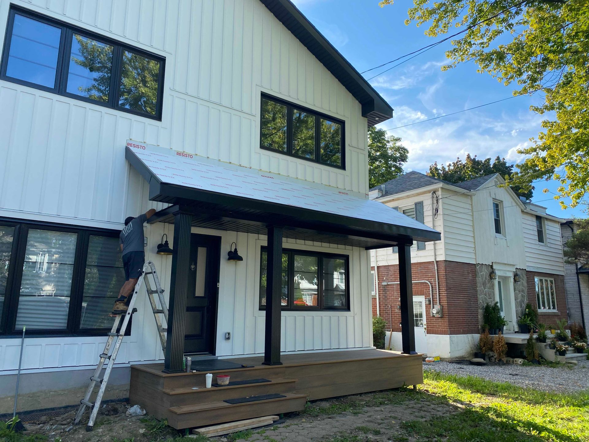 Maison blanche avec des boiseries noires, porche en construction, personne sur une échelle.