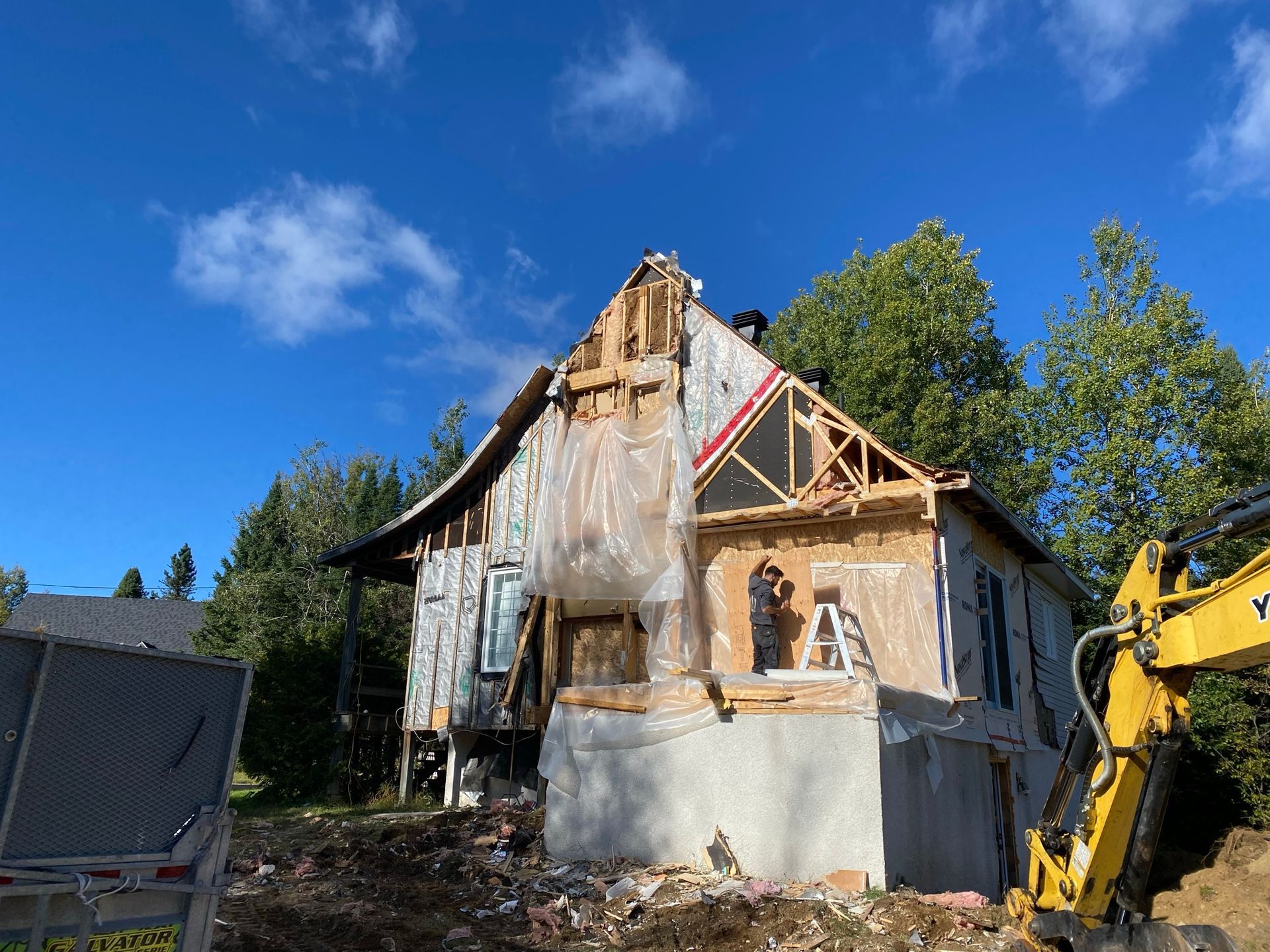 Maison en démolition, pelleteuse en vue, ciel bleu dégagé.
