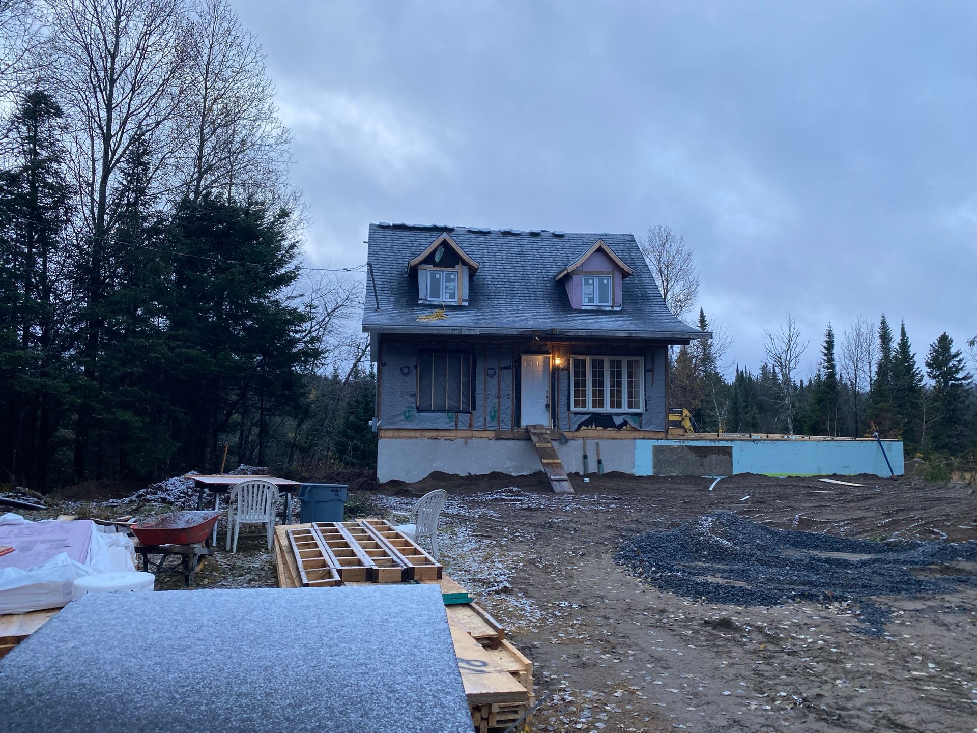 Maison en construction aux fondations apparentes, entourée de matériaux de construction par temps nuageux.