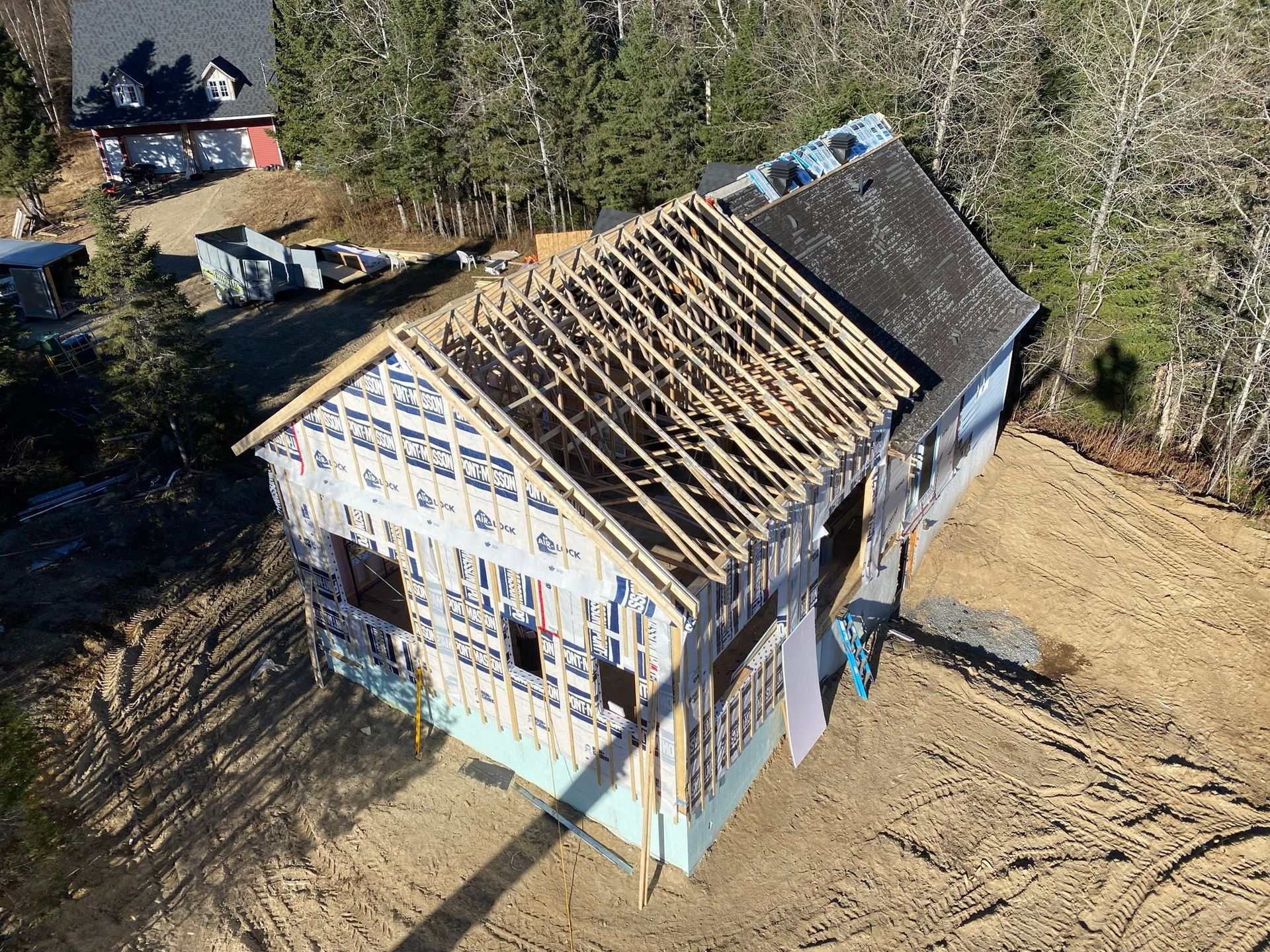 Chantier : structure en bois d'une maison avec toiture partiellement installée et terre environnante.