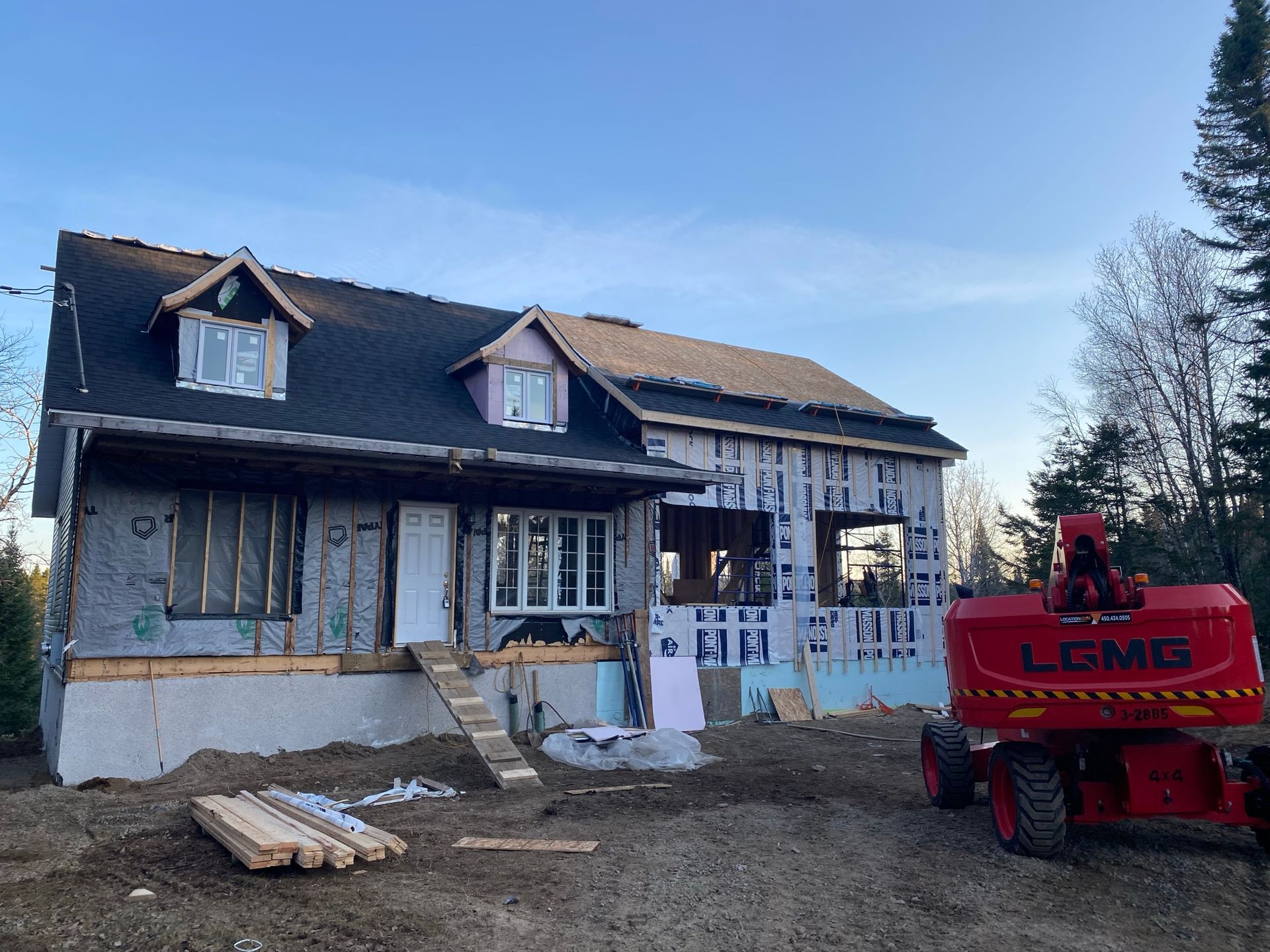 Maison en construction avec charpente apparente et échafaudages ; ciel lumineux.