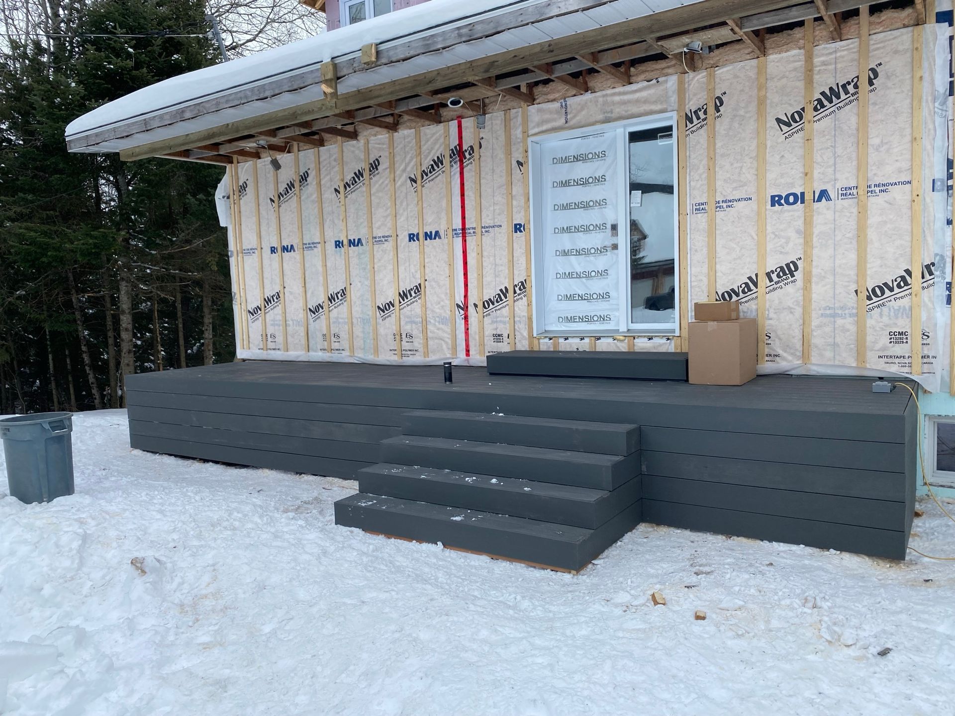 Vue extérieure d'une maison en construction avec une terrasse et des marches grises dans un environnement enneigé.