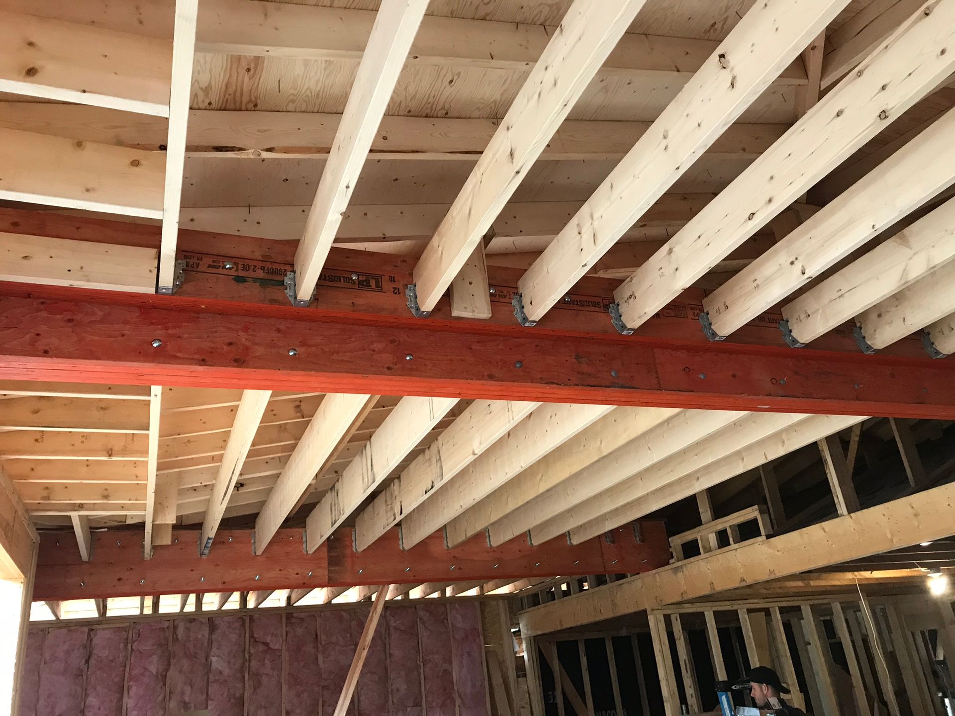 Plafond en bois en construction, avec poutres apparentes soutenues par une poutre métallique rouge.