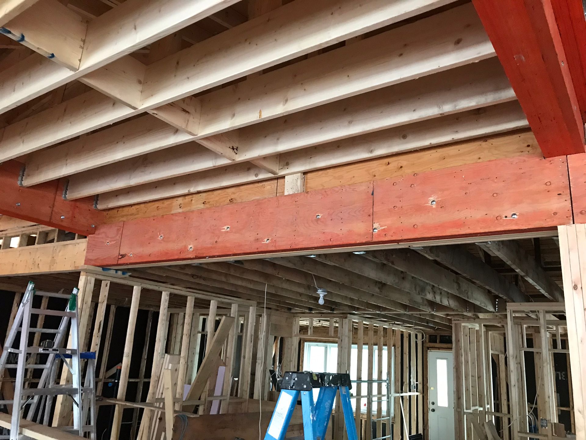 Vue intérieure d'un bâtiment en construction, montrant la charpente en bois apparente, notamment les poutres, les solives et les montants ; une échelle bleue est visible.