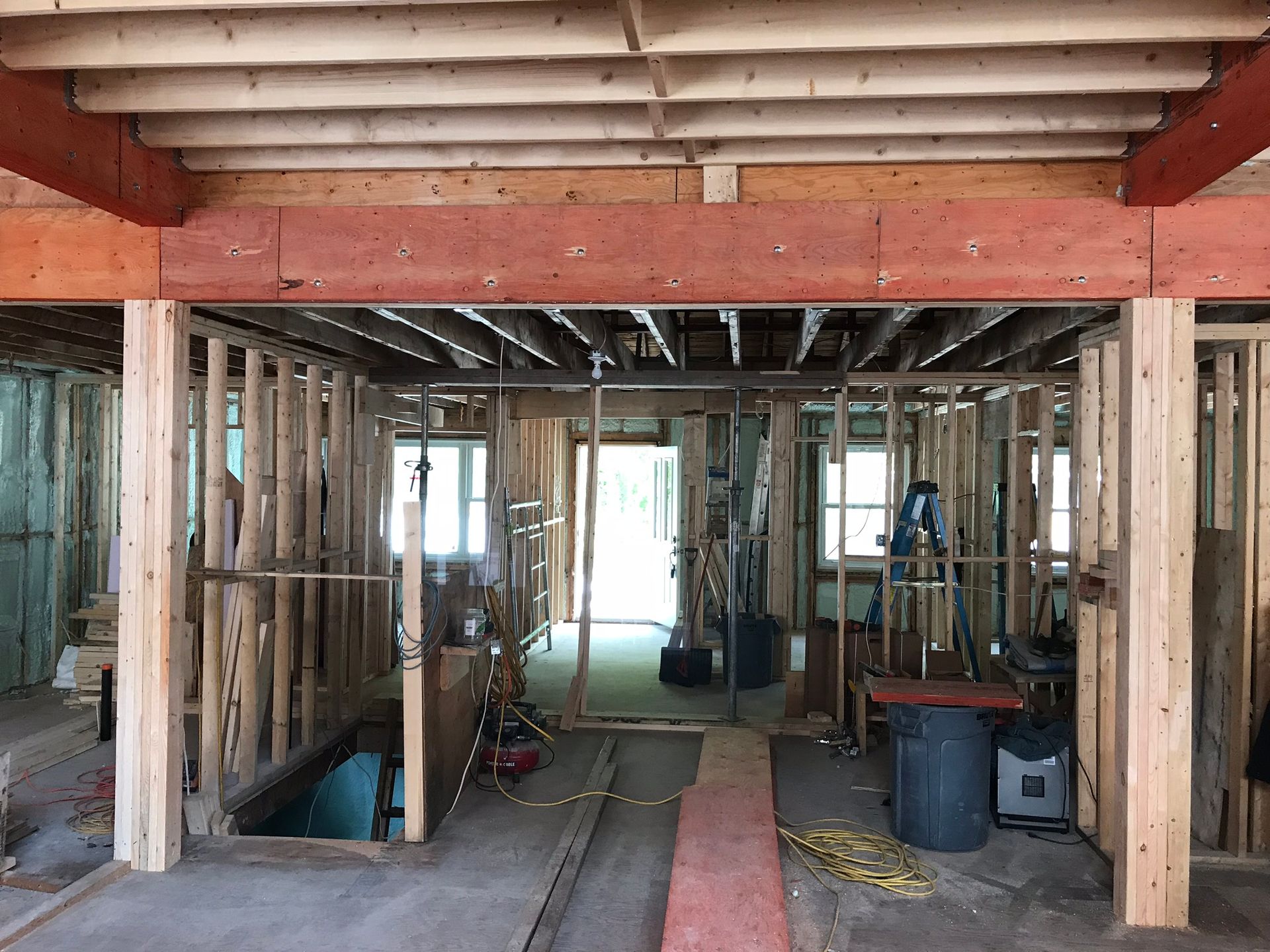 Intérieur d'un bâtiment en construction, montrant la charpente en bois apparente et les poutres de soutien.