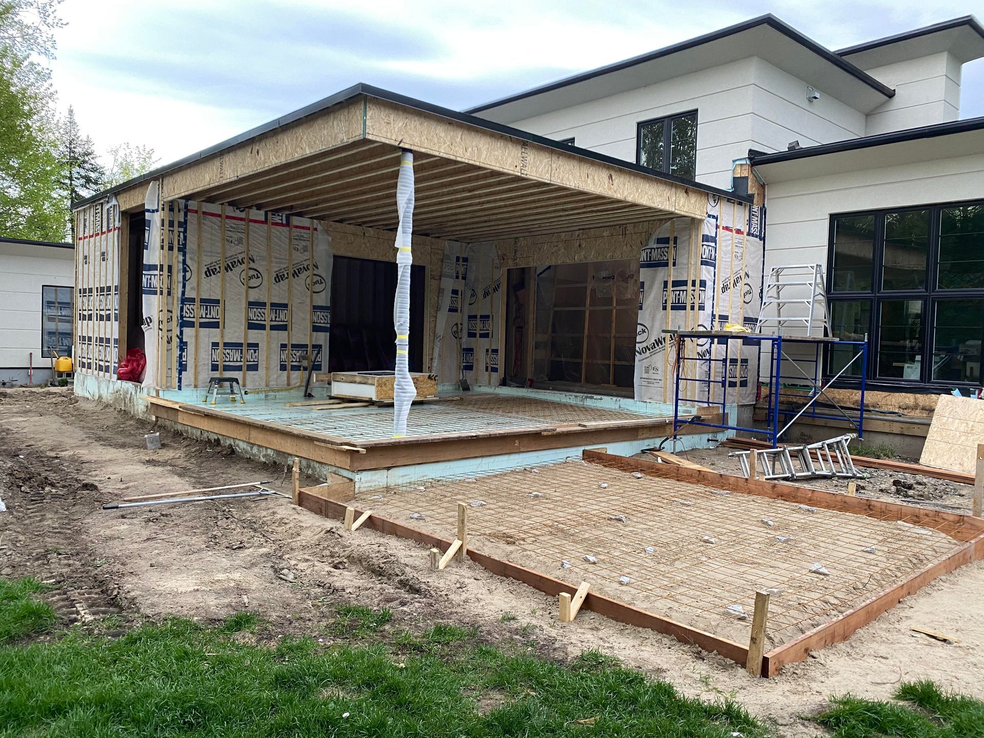 Chantier de construction : extension d’une maison en cours de réalisation, avec charpente, coffrages en béton et revêtement visibles.