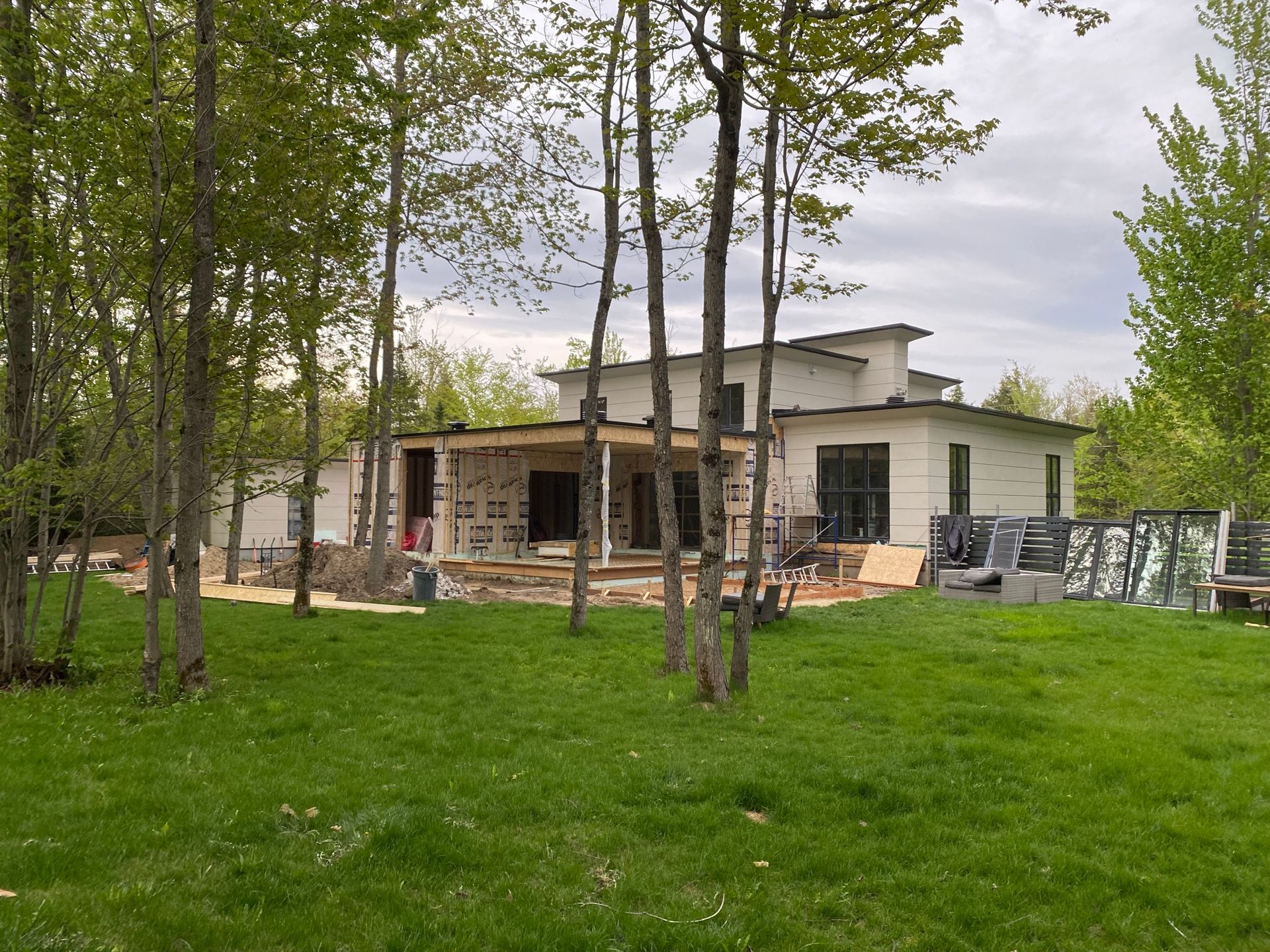 Maison en construction dans une zone boisée, entourée d'herbe verte et d'arbres.