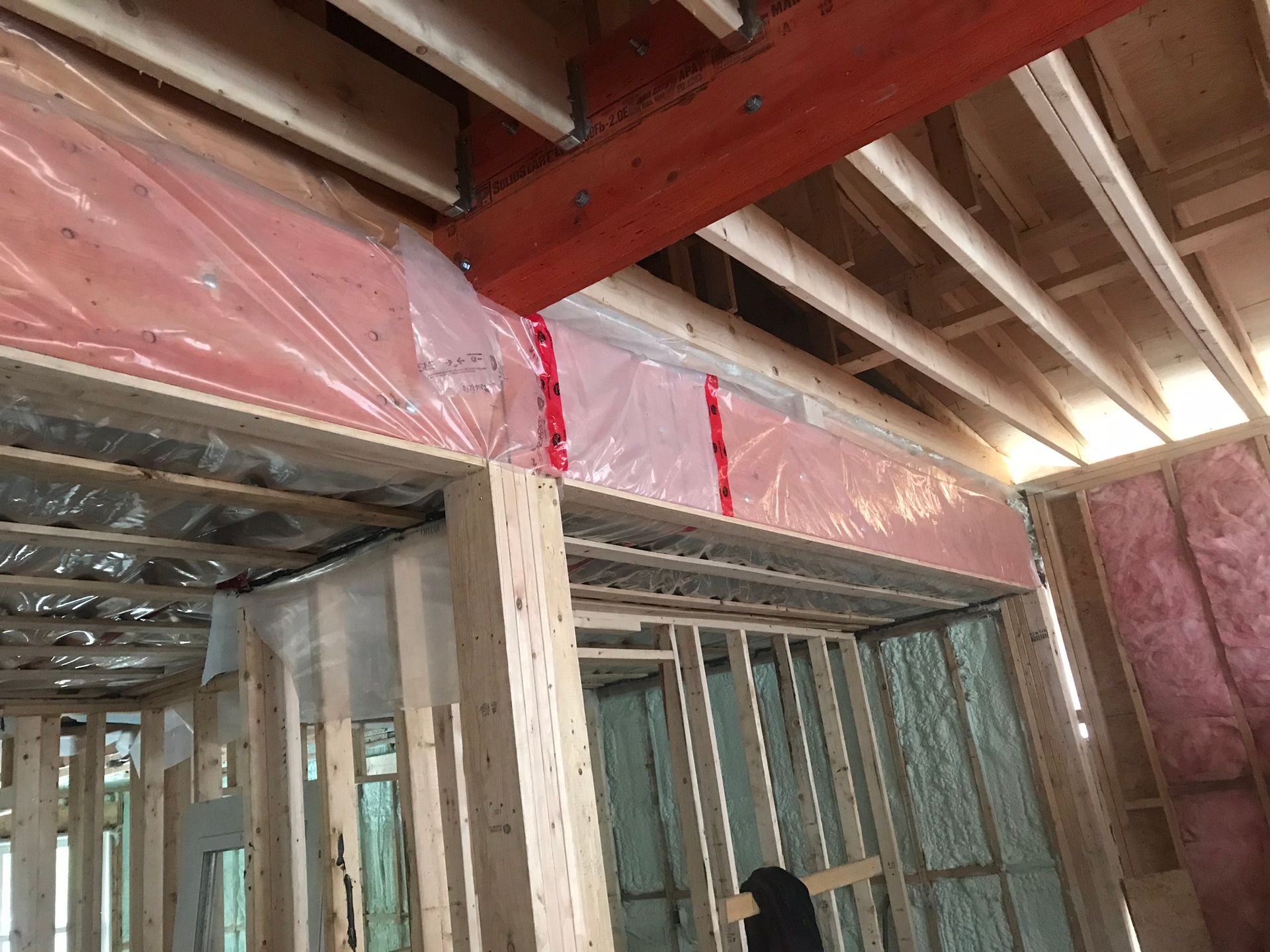 Encadrement d'une porte dans un bâtiment en construction. On aperçoit l'isolant rose ainsi que des poutres en bois.