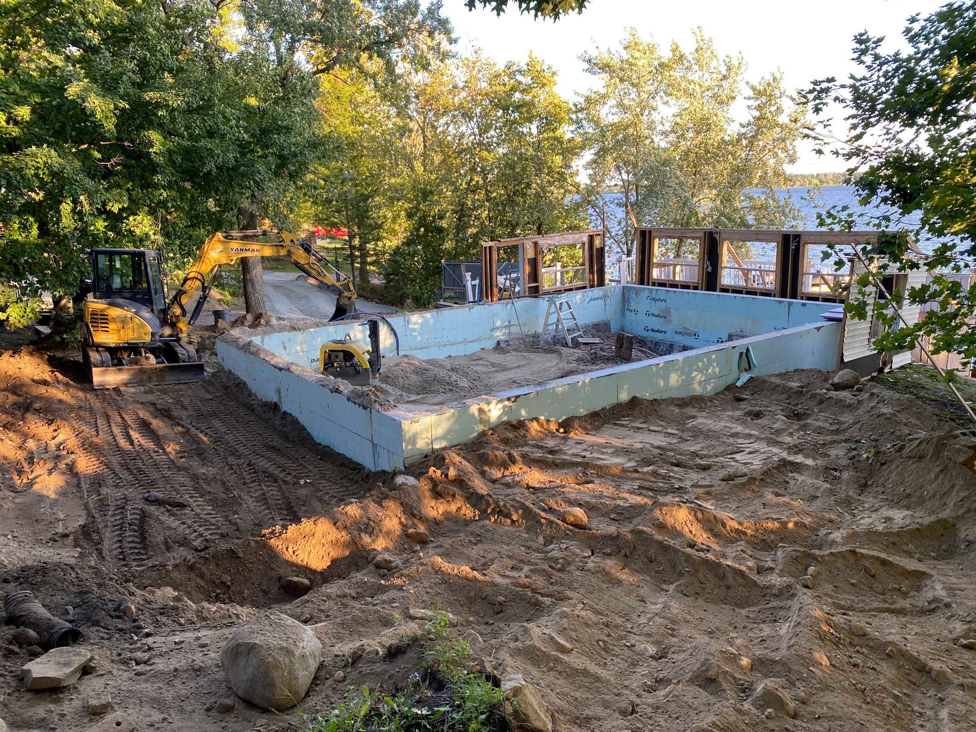Chantier de construction avec excavatrice et fondations, terre et arbres.