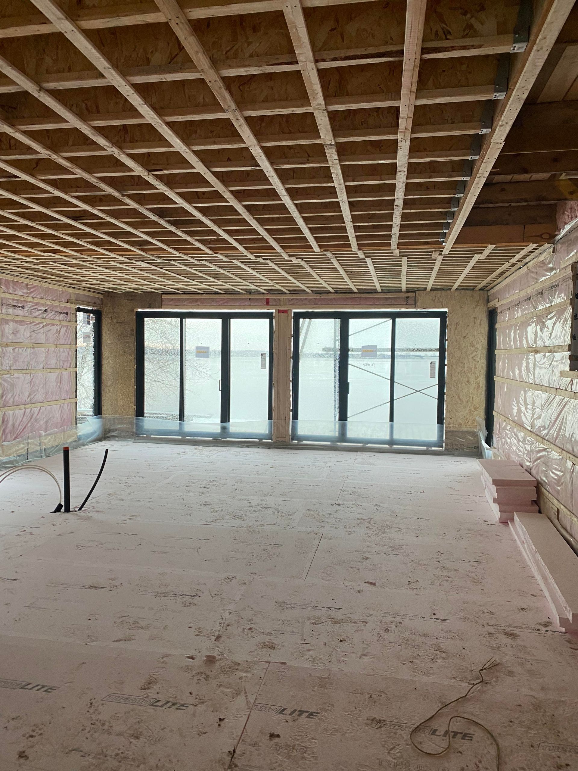 Intérieur d'un bâtiment en construction, montrant la structure du plafond en bois, les fenêtres et l'isolation apparente.