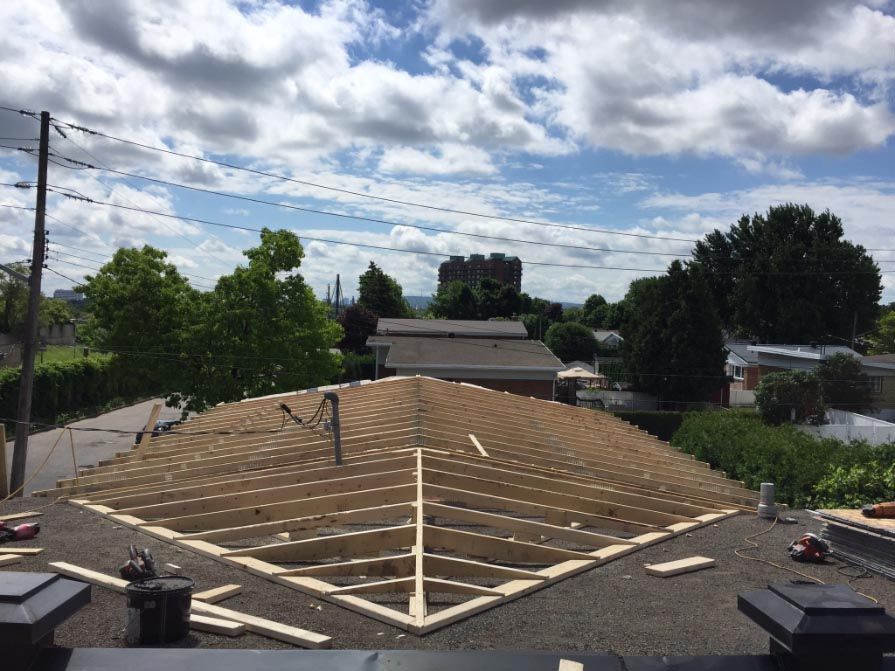 Construction d'une charpente de toit en bois sur un toit avec un ciel nuageux en arrière-plan.