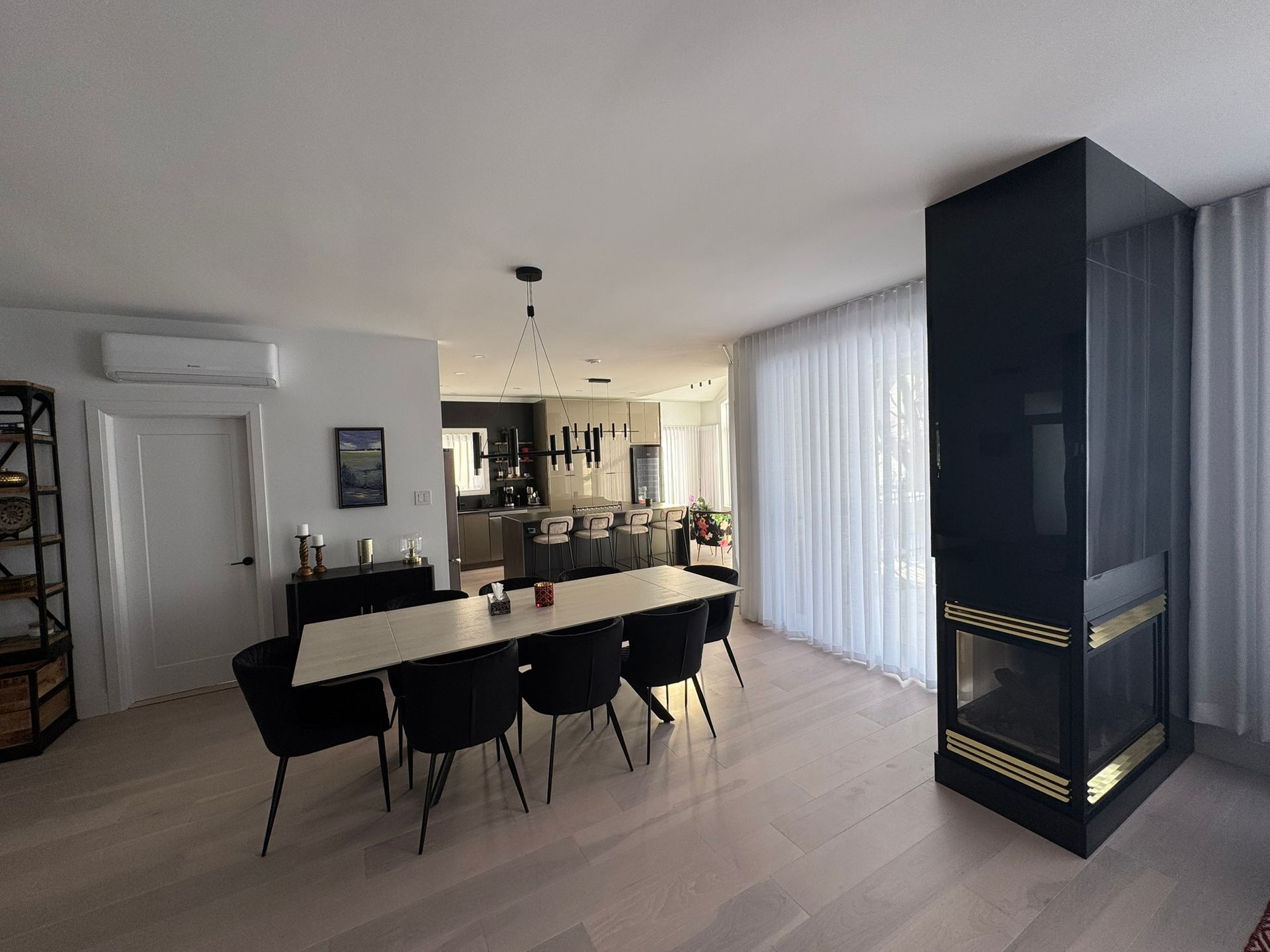 Salle à manger avec une longue table et des chaises noires, cheminée noire et parquet clair.