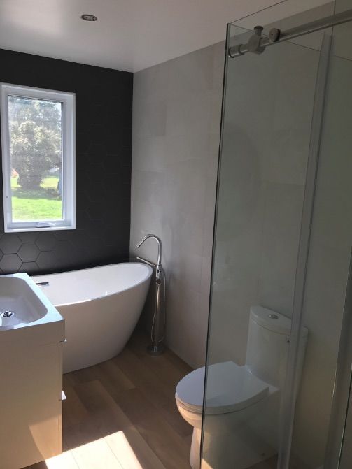 Salle de bains moderne avec baignoire, douche et toilettes blanches, avec une fenêtre et un mur d'accent foncé.