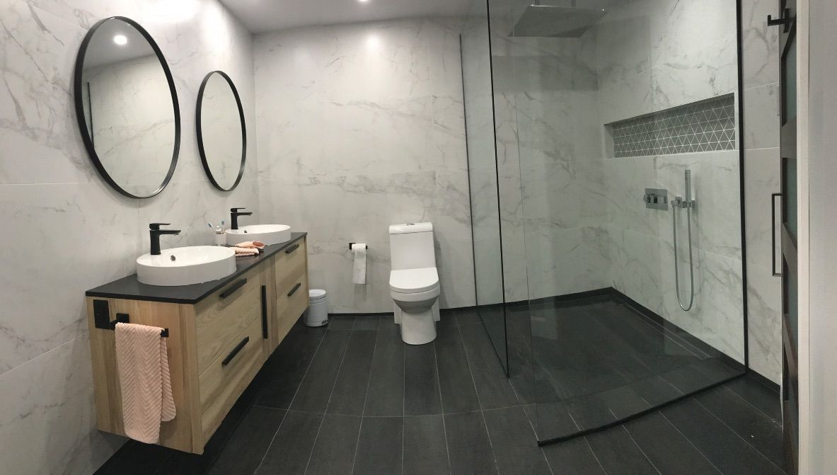 Salle de bains moderne avec murs en marbre, meuble-lavabo en bois, deux miroirs et douche en verre.