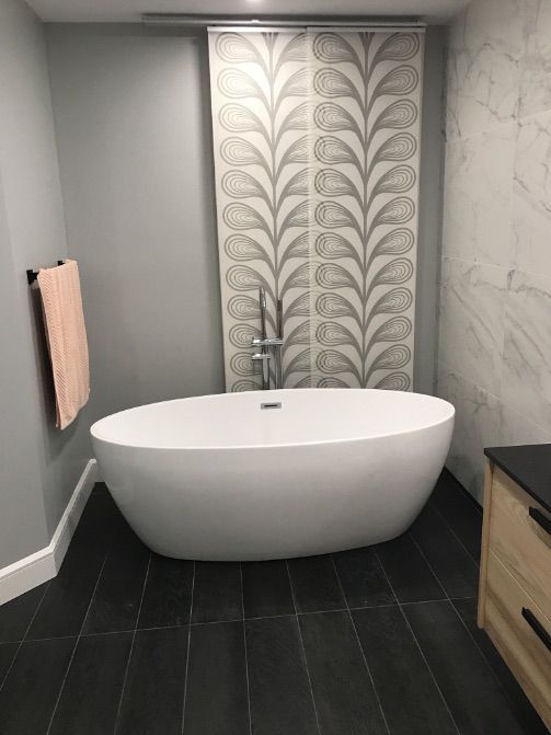 Salle de bains moderne avec baignoire blanche, sol carrelé noir, mur carrelé à motifs et murs gris.