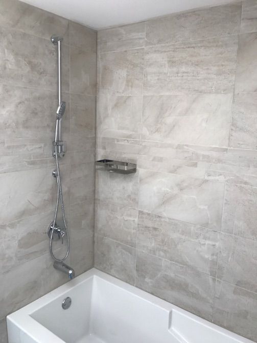 Salle de bains avec baignoire blanche, murs carrelés et robinetterie de douche argentée.