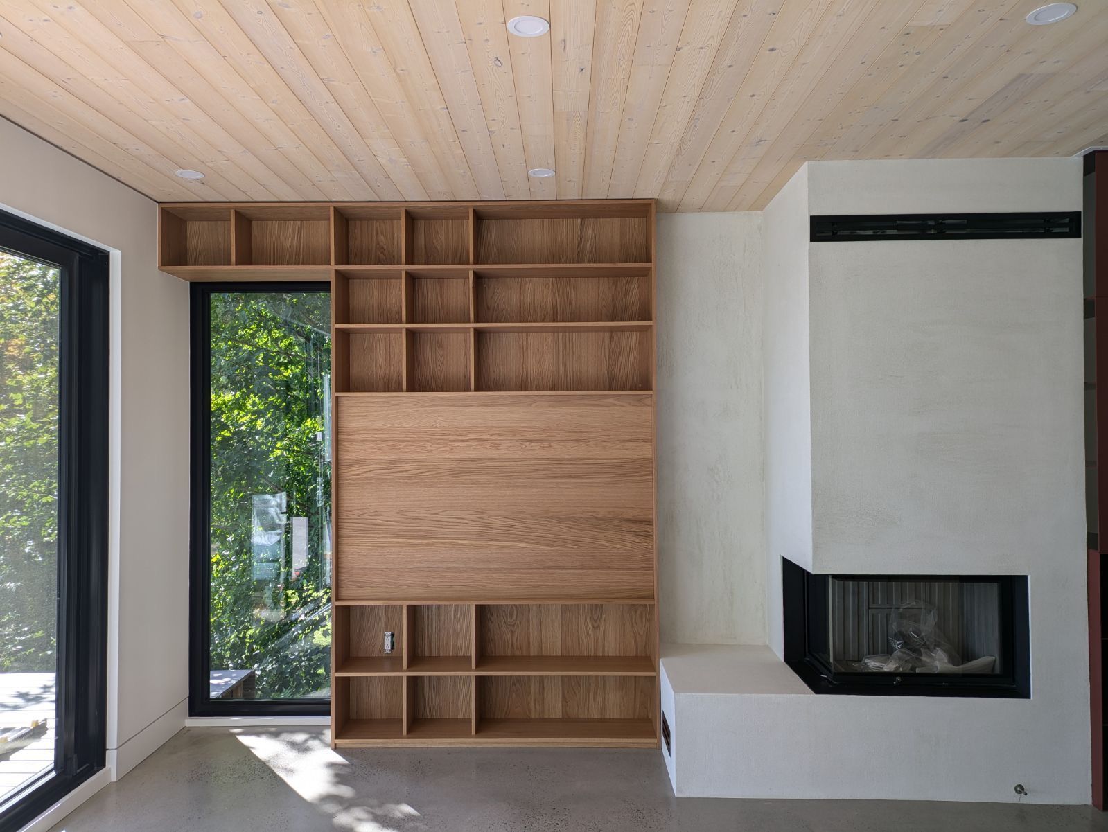 Salon moderne avec étagères en bois, cheminée et grande fenêtre.