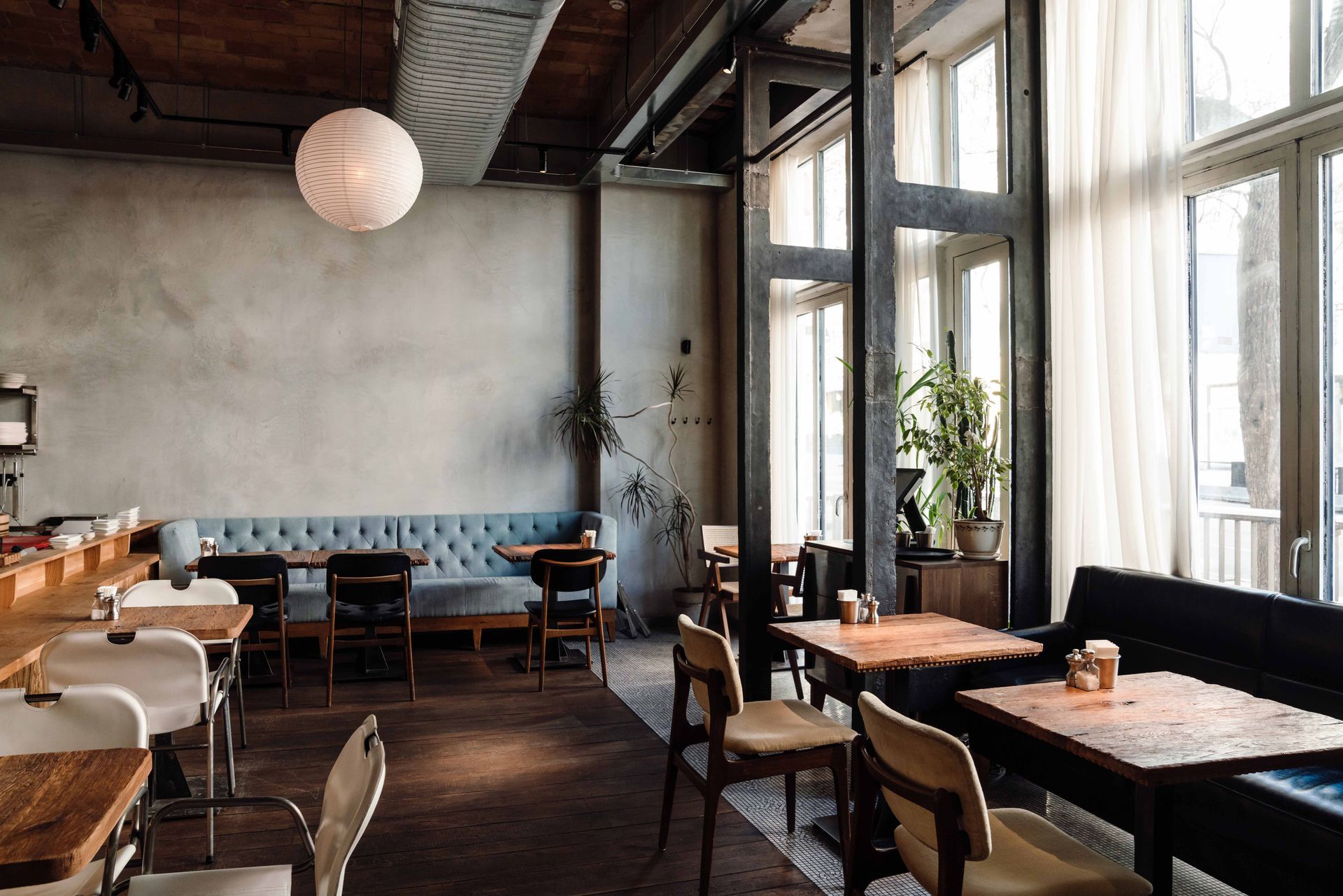 Vue intérieure d'un café avec tables, chaises et grandes fenêtres. Éclairage tamisé et tons neutres.