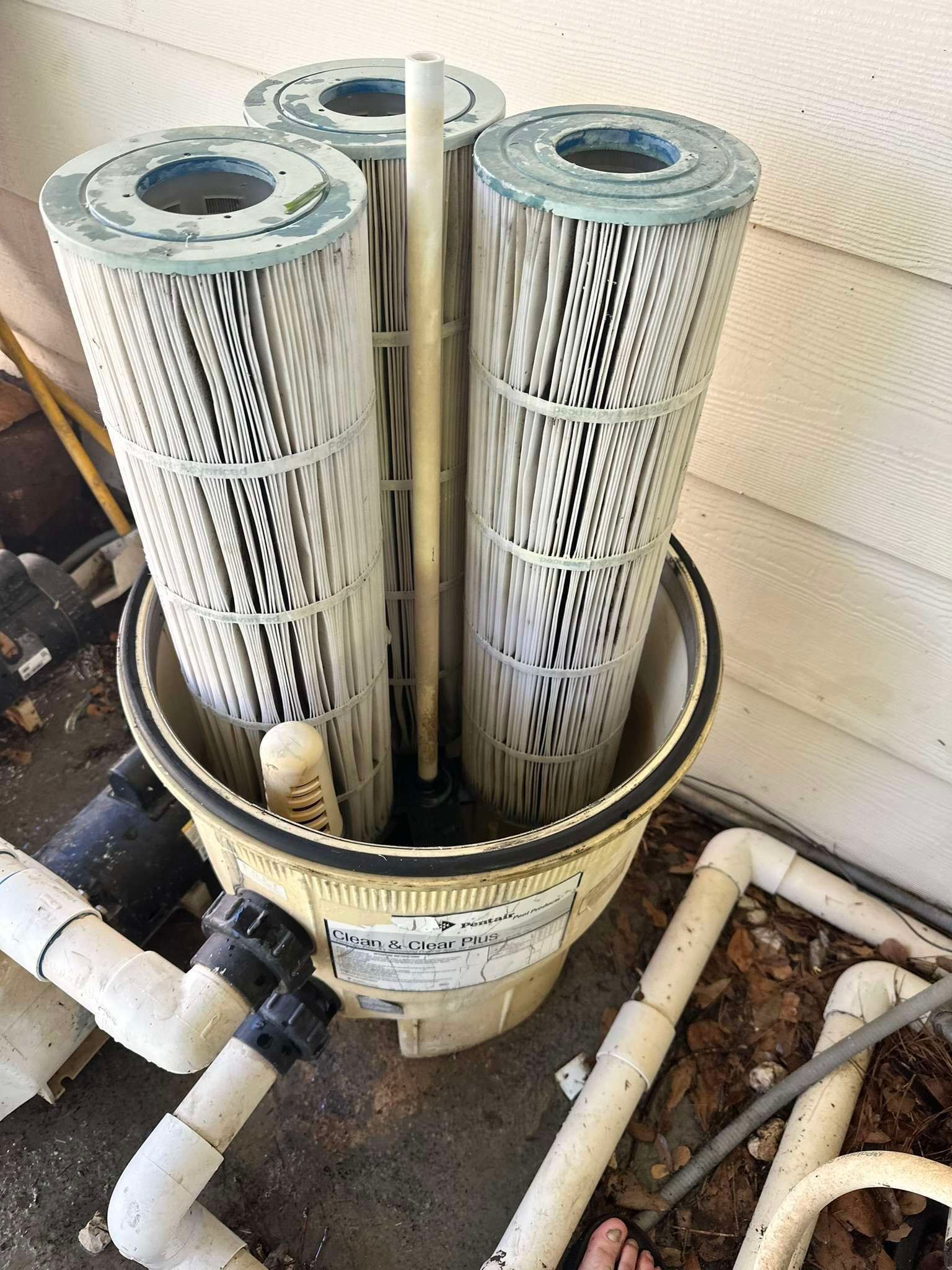 Pool filter with three cartridge filters inside a beige housing, connected to white pipes.