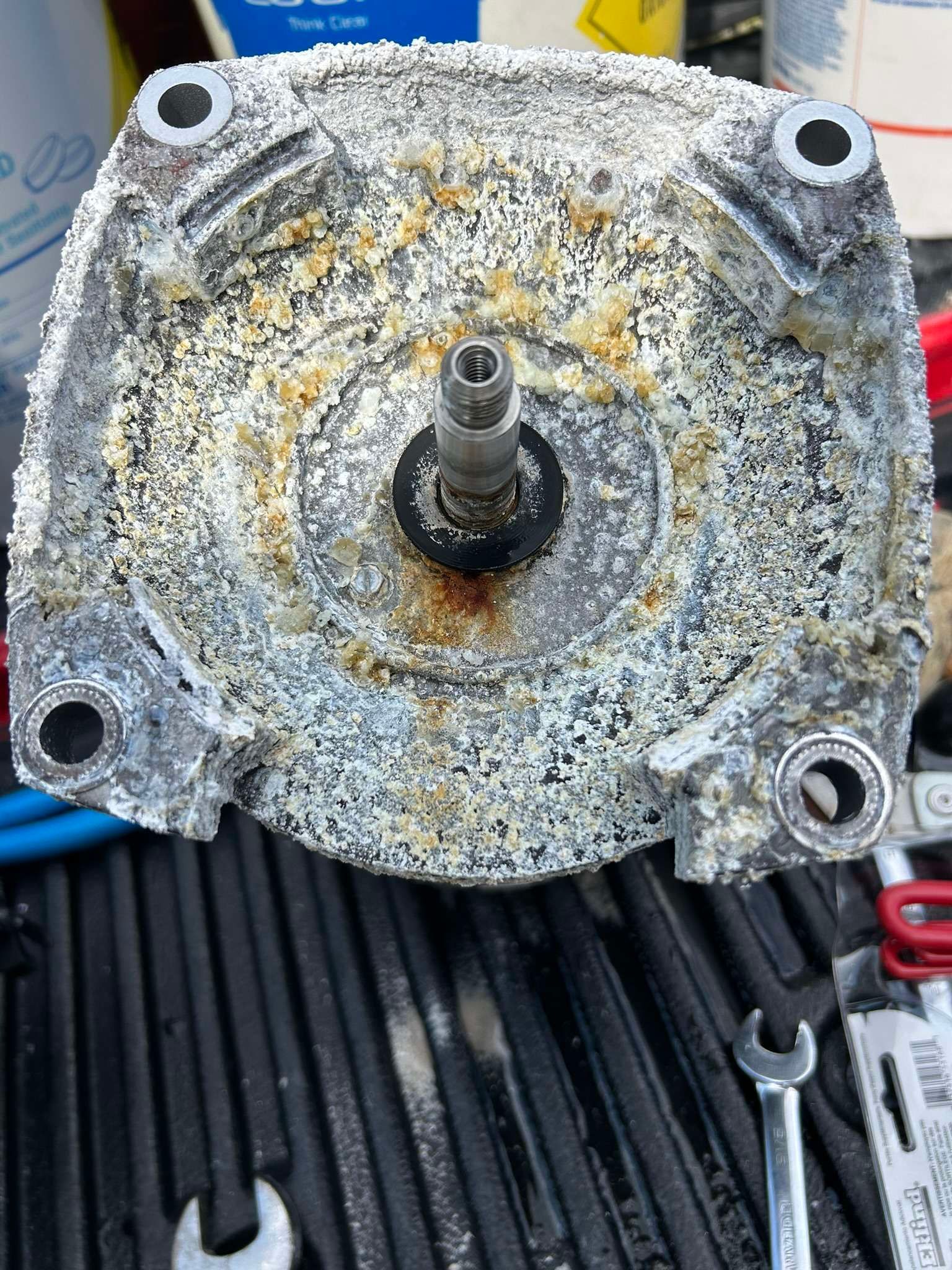 Aluminum motor housing covered in white residue, with central shaft, and bolt holes.