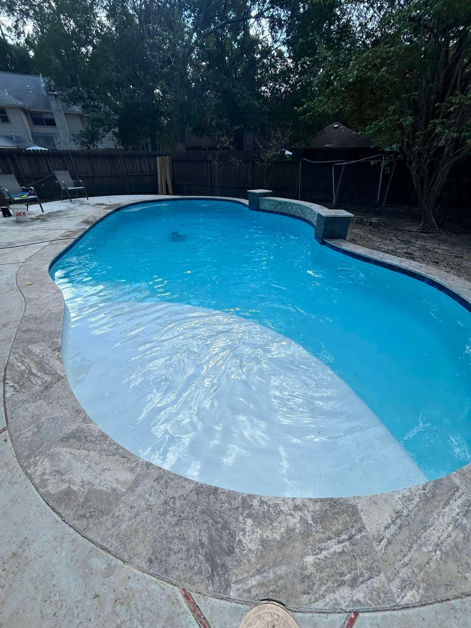 Swimming pool with blue water and gray concrete edging, surrounded by trees.