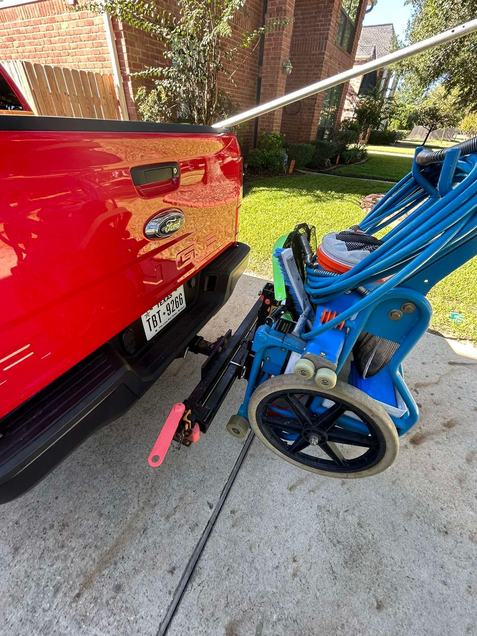 Red truck backed up to a blue power washer on a driveway.