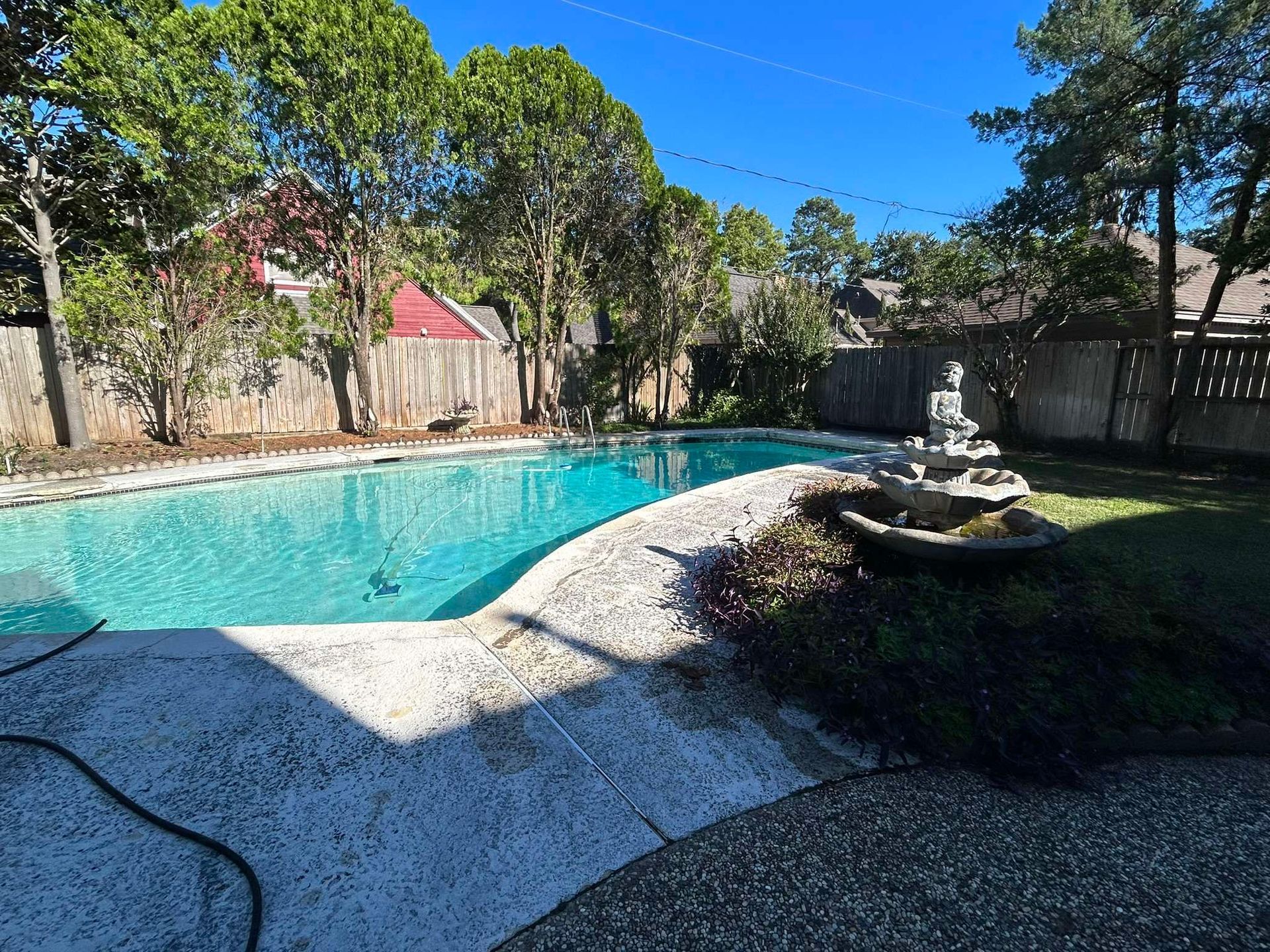 Backyard pool with stone path, fountain, and wooden fence on a sunny day.