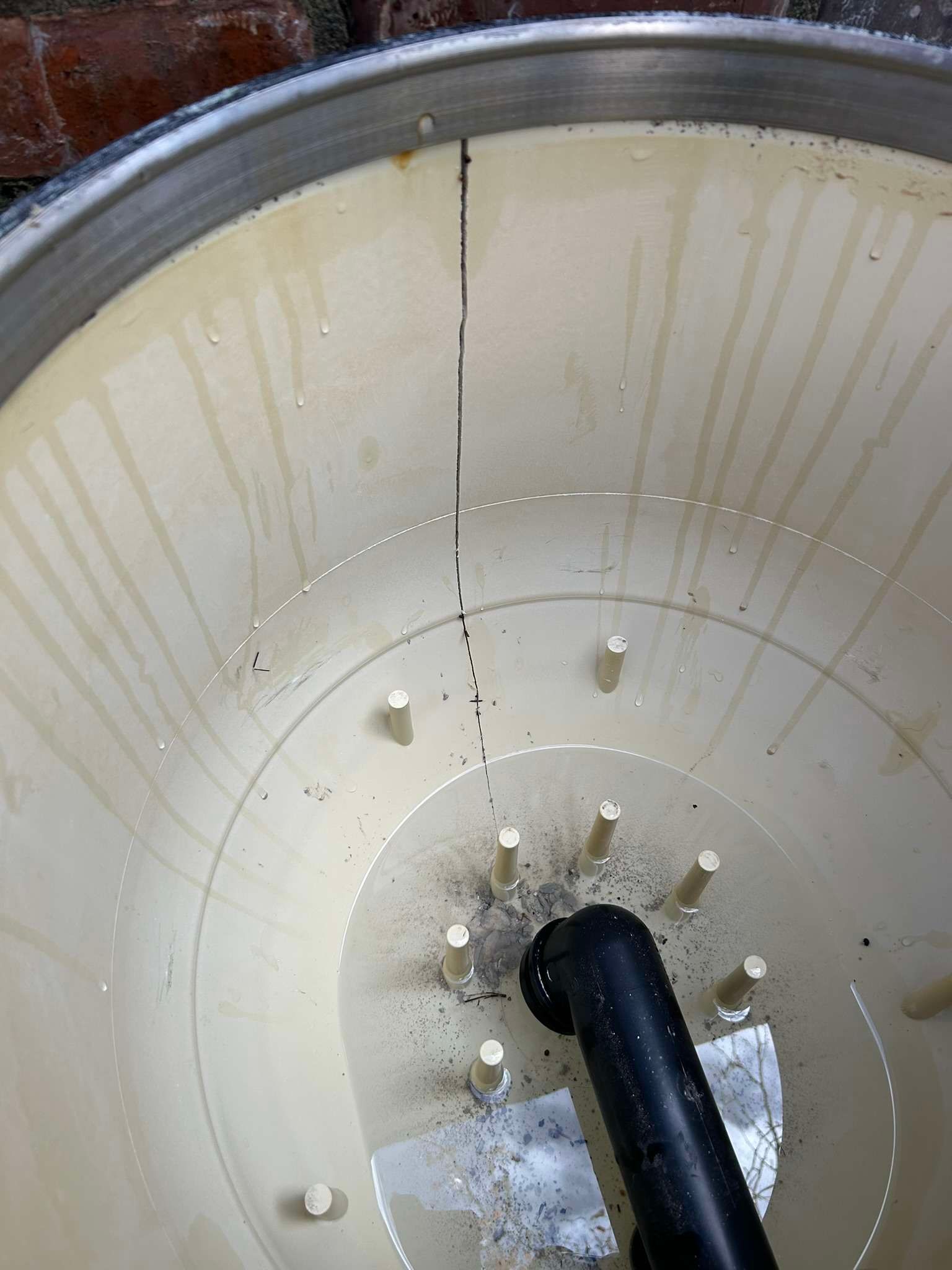 Inside view of a cracked, light-colored tank with a dark pipe at the bottom.