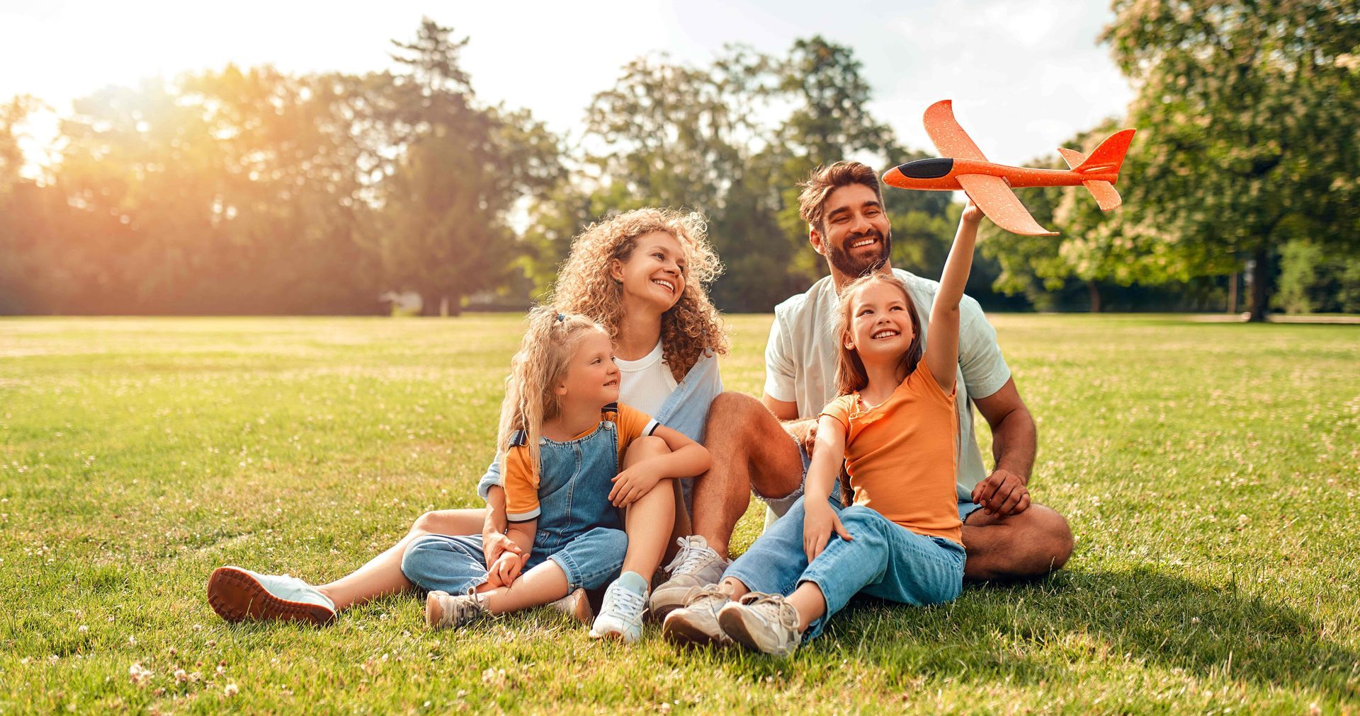 a family is sitting on the grass in a park playing with a toy airplane