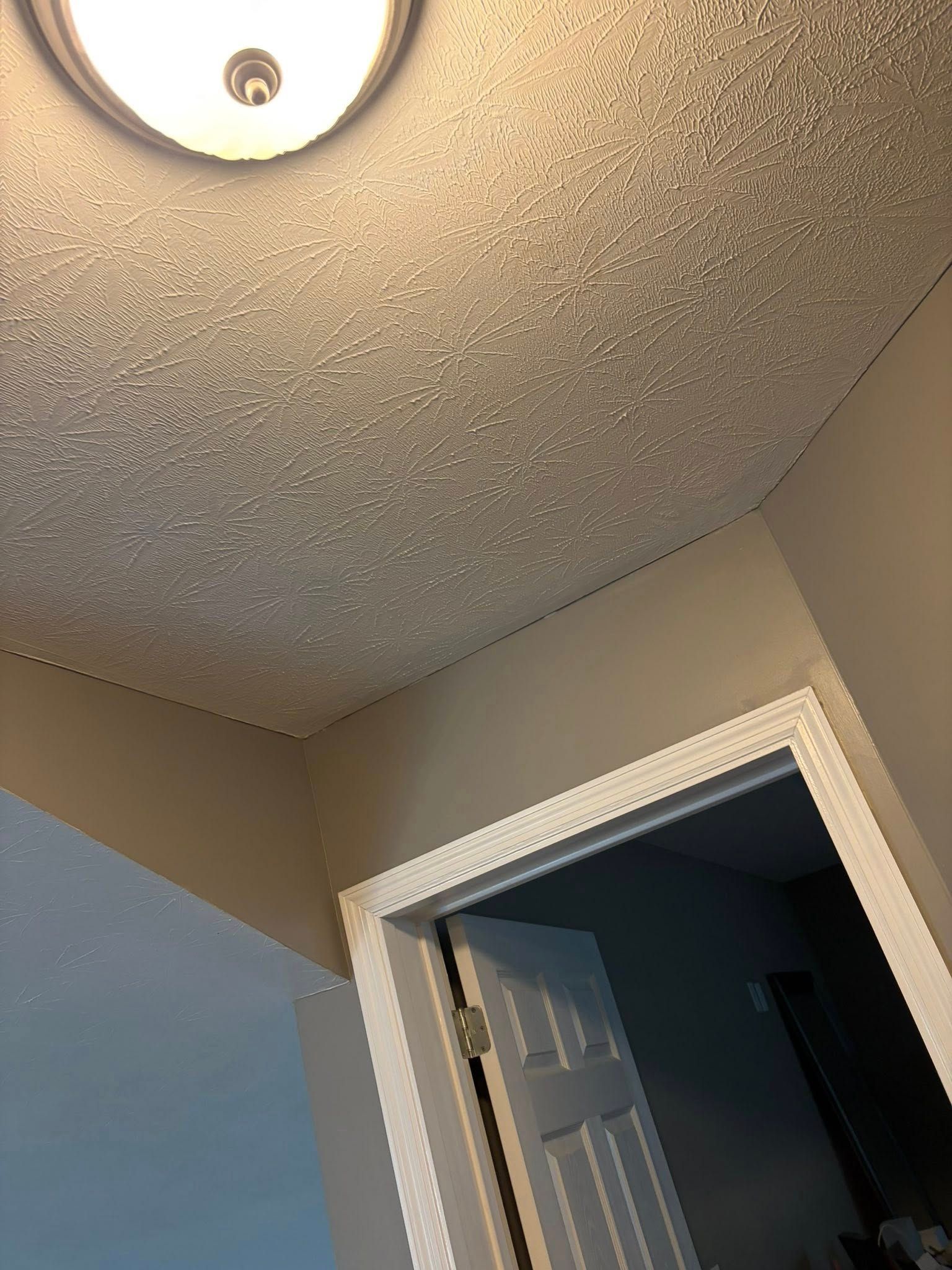 Upward view of a textured ceiling with a lit flush-mount light above an open doorway.