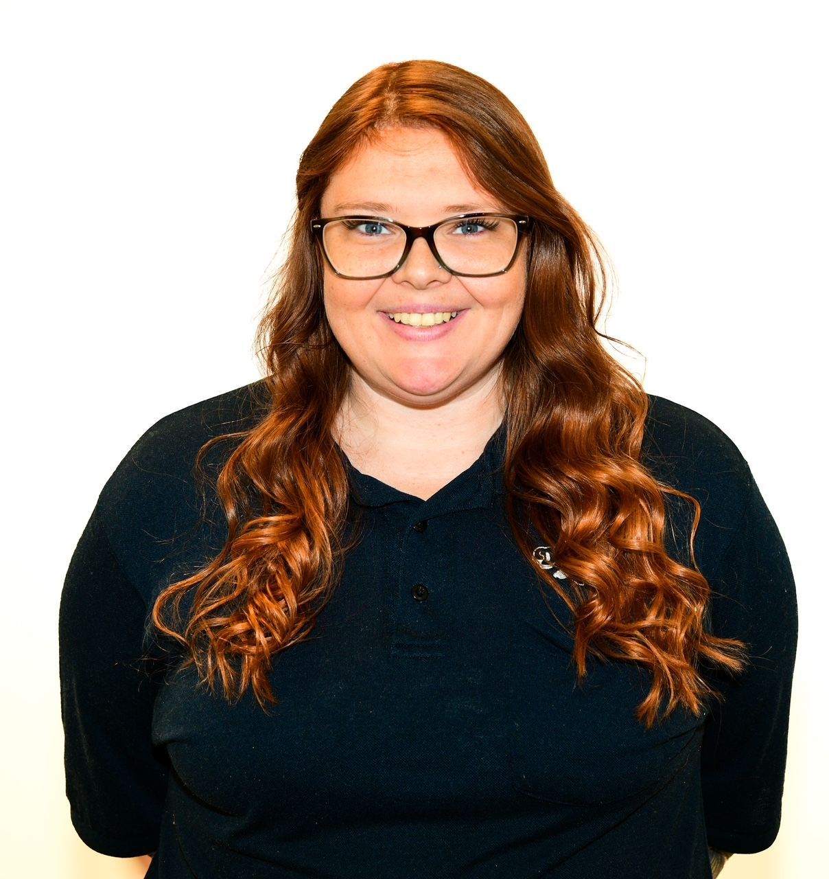 Woman with red hair and glasses smiles, wearing a dark blue shirt against a white background.