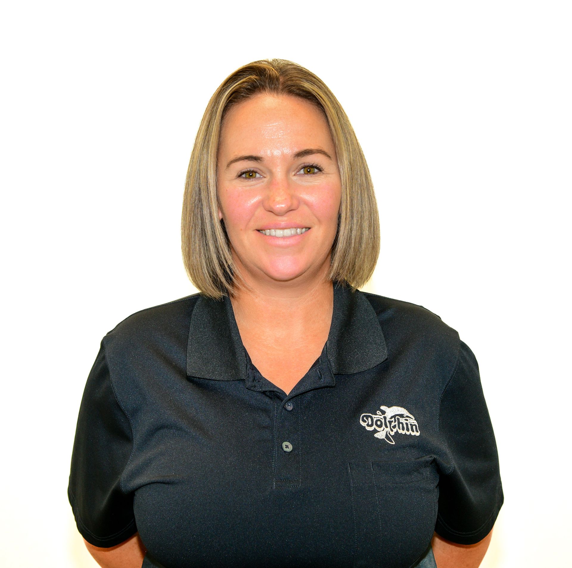 Woman in dark polo shirt, smiling, looking at the camera. Company logo on shirt.
