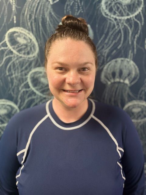 A woman in a blue shirt is smiling in front of a wall with jellyfish painted on it