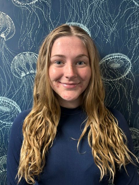 A woman wearing glasses and a blue shirt is standing in front of a wall with jellyfish on it