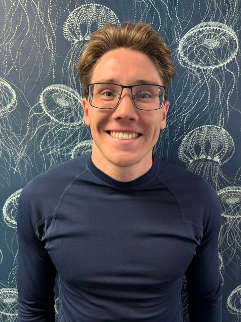 A woman in a blue shirt is smiling in front of a wall with jellyfish on it