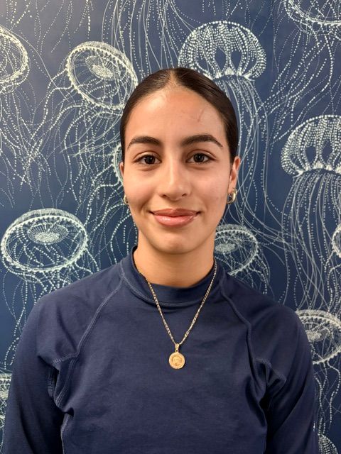 A woman wearing a blue shirt and a necklace is smiling in front of a jellyfish wallpaper.