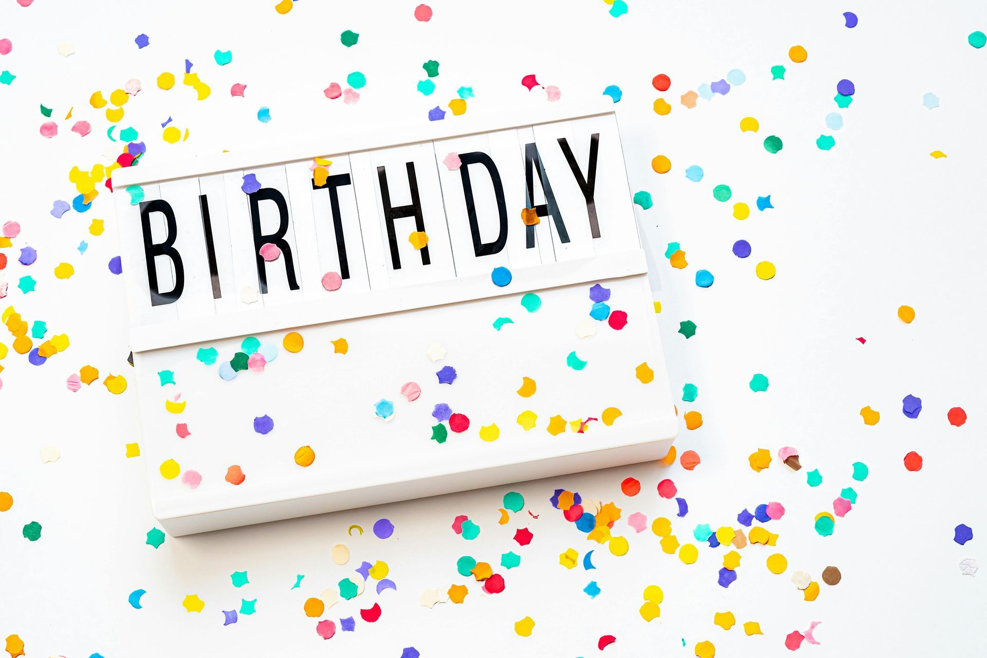 A birthday sign surrounded by colorful confetti on a white background.