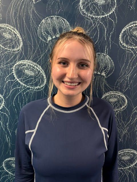 A woman in a blue shirt with jellyfish on the wall behind her