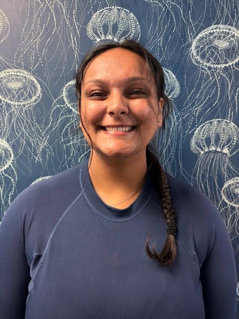A man in a blue shirt is smiling in front of a wall with jellyfish on it