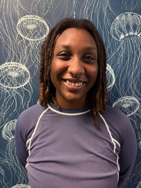 A woman in a blue shirt is smiling in front of a wall with jellyfish on it