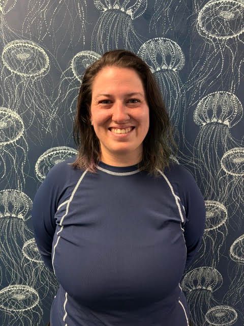 A woman in a blue shirt is smiling in front of a wall with jellyfish on it.