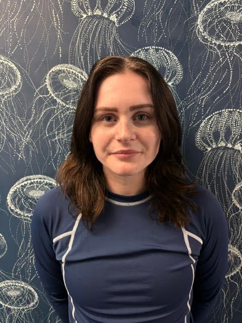 A woman in a blue shirt is smiling in front of a wall with jellyfish on it.